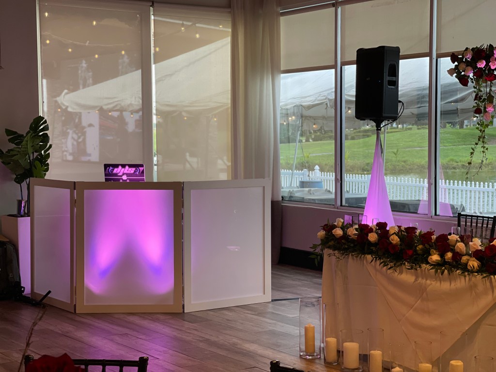 Purple-lit DJ booth with speaker and floral reception table