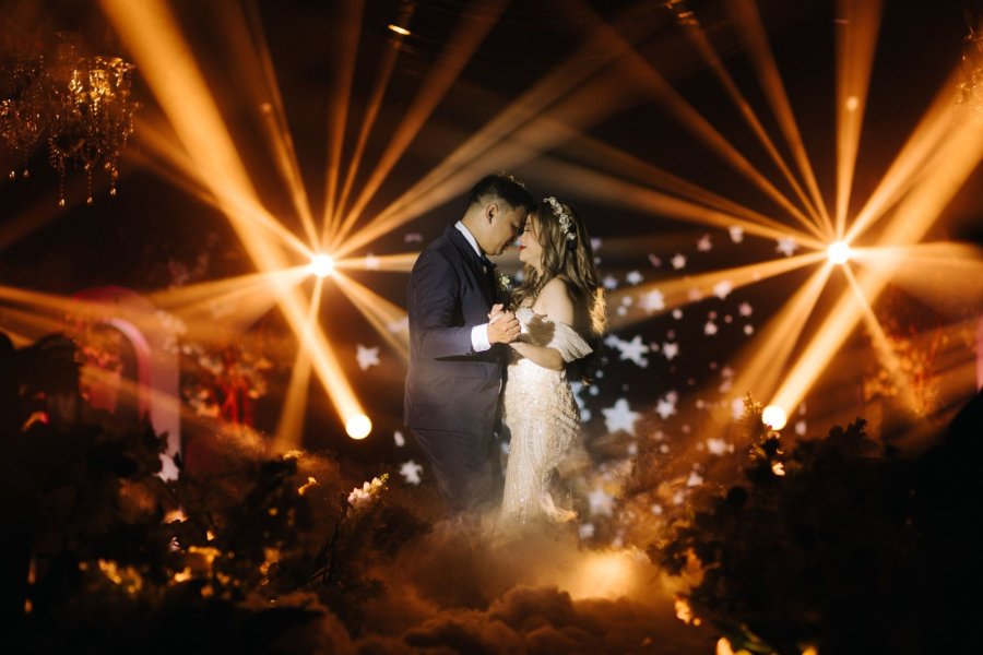 Bride and groom sharing their first dance under golden beam lights and low fog