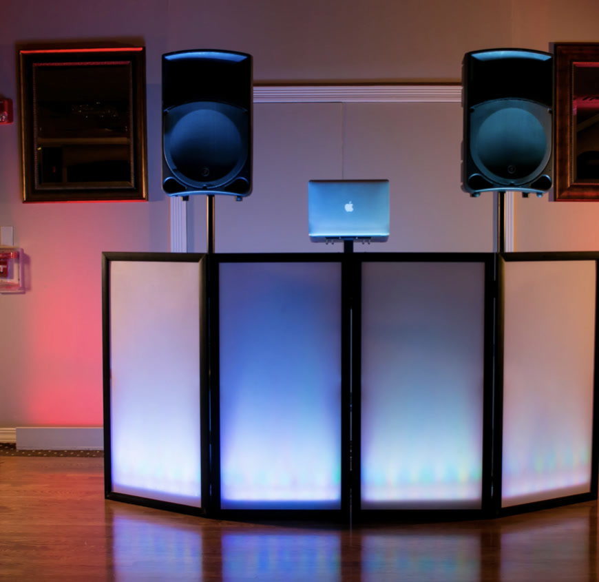 Illuminated DJ facade with speakers and laptop in a ballroom with color uplighting